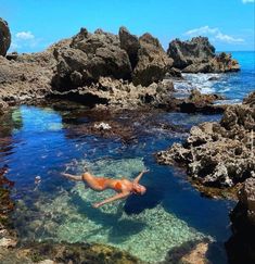 a person swimming in the ocean near some rocks and clear blue water on a sunny day