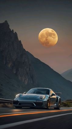 a blue sports car driving down the road in front of a full moon and mountains