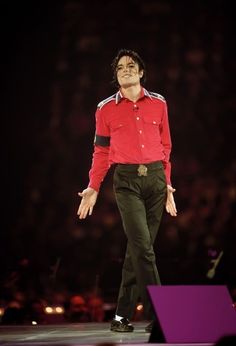 a male in a red shirt and black pants is walking with his hands out to the side