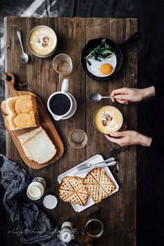 a table topped with plates of food next to cups of coffee and other items on top of a wooden board