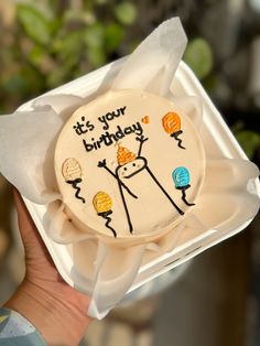 a hand holding a decorated birthday cake in a box