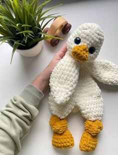 a crocheted stuffed bird is being held by a person's hand next to a potted plant