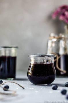 two jars filled with blueberry jam sitting on top of a table next to berries