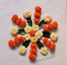 an arrangement of orange and white flowers arranged on a marble surface with text that reads rupa's rangoli