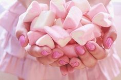 a woman's hands with pink and white manicures holding candy - shaped marshmallows