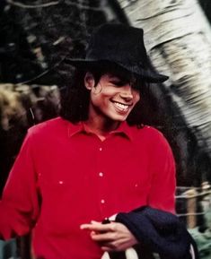 a man in a red shirt and black hat smiles while holding a white frisbee