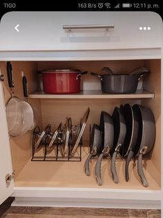 an open cabinet with pots and pans on the bottom shelf, next to other kitchen utensils