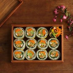 there are many sushi rolls in the box on the table next to some flowers