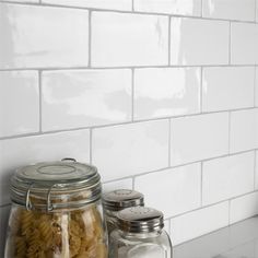 two glass jars filled with pasta sitting on top of a counter next to a white tiled wall