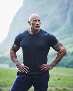 a man with his hands on his hips standing in front of a grassy field and mountains