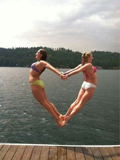 two women in bikinis jumping into the water from a dock with their hands together