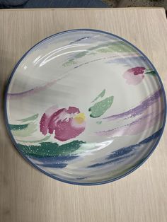 a plate with flowers painted on it sitting on a wooden table next to a knife and fork