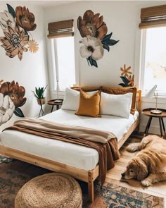 a dog laying on the floor next to a bed in a room with flowers painted on the walls