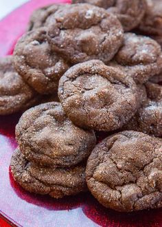 chocolate cookies are piled on top of each other in a red plate, with powdered sugar sprinkles