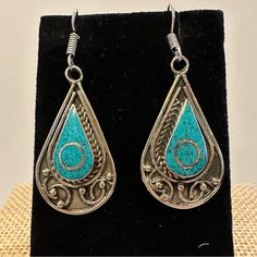 a pair of silver and turquoise earrings on a black velvet stand with a white background