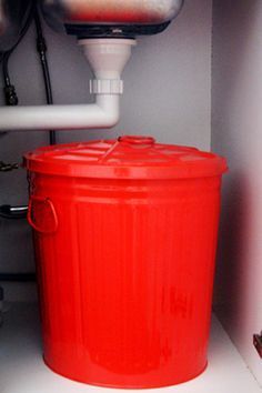 a red bucket sitting on top of a white counter next to a faucet