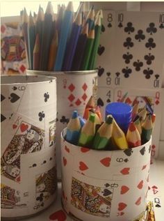 pencils and crayons are sitting in tins on a desk next to playing cards