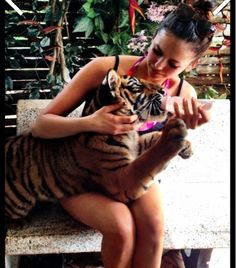 a woman sitting on a bench holding a tiger cub