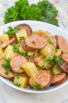 a bowl filled with sausage and potatoes on top of a white plate next to parsley