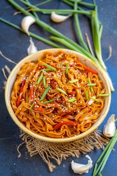 a bowl filled with noodles and vegetables on top of a blue tablecloth next to garlic