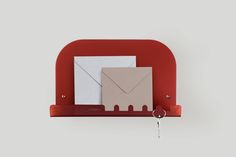 a red shelf with two envelopes and a key hanging from the hook on it