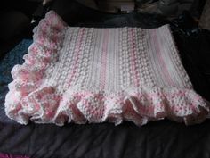 a crocheted blanket is laying on top of a bed with pink and white ruffles