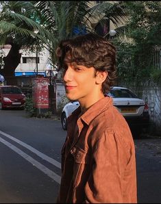 a young man standing on the side of a road next to a tree filled street