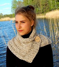 a woman standing next to a lake wearing a scarf