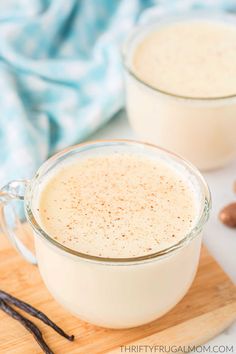 two glasses of eggnog on a cutting board with cinnamons and cloves