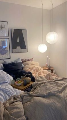 an unmade bed in a bedroom with two lamps hanging above it and pictures on the wall