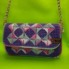 a purple purse with pink, white and green designs on it sitting on a green surface