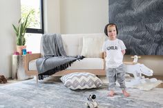 a little boy standing in front of a couch with toys on the floor next to him