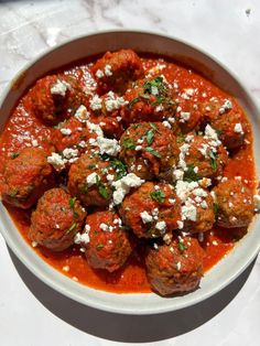 a white bowl filled with meatballs covered in marinara sauce and feta cheese