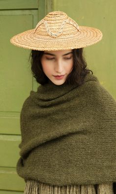 a young woman wearing a straw hat and green shawl standing in front of a green door