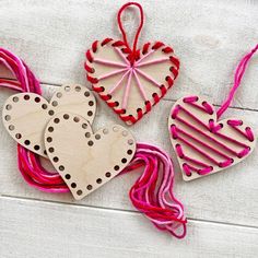 three wooden heart ornaments with pink and red thread on white wood planks, one hanging from the ceiling