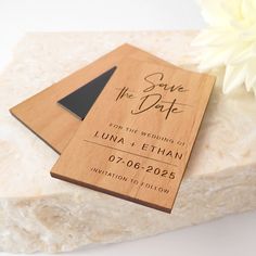 a wooden save the date card sitting on top of a white marble block next to a flower