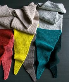 four different colored knitted items are lined up on a black surface with one folded over the other