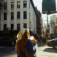 a woman standing on the side of a road next to tall buildings and traffic lights