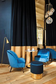 a living room with two blue chairs and a round table in front of black drapes