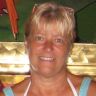 a woman with blonde hair and blue tank top smiling at the camera while standing in front of a parrot cage