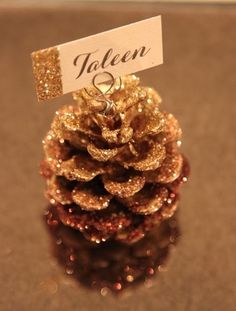 a small pine cone with a name tag on it's top and some glitter around the base