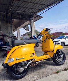 a yellow scooter is parked in front of a gas station with other cars