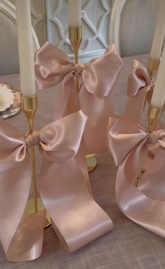 three candles with pink bows on them sitting on a table next to plates and napkins