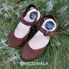 Discover the artistry of handcrafted women's clogs, meticulously created with a NATURAL LEATHER upper and WOOD sole. These durable and stylish shoes are a testament to Swedish quality and design.  Each pair is carefully crafted from the finest materials, ensuring exceptional quality. The wooden sole, expertly carved from a single piece of alder tree, boasts an ergonomic shape. This soft yet sturdy material is dried for up to 6 months before being transformed into a fashionable sole. Brown Closed Toe Sandals With Heel Strap, Brown Sandals With Heel Strap And Round Toe, Brown Closed Toe Walking Sandals, Brown Sandals With Rubber Sole And Flat Heel, Brown Closed Toe Sandals For Walking, Brown Flat Heel Sandals With Rubber Sole, Brown Mules With Buckle Closure And Flat Heel, Brown Flat Heel Heels With Rubber Sole, Closed Toe Sandals With Rubber Sole For Walking