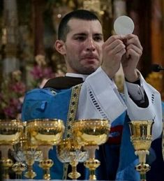 the priest is holding his chalice in front of some gold goblets and candles