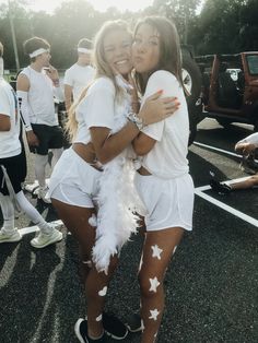 two young women hugging each other in the middle of a parking lot at a sporting event