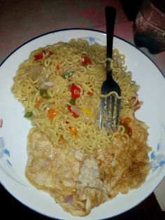 a plate with noodles, meat and vegetables next to a fork on the table top