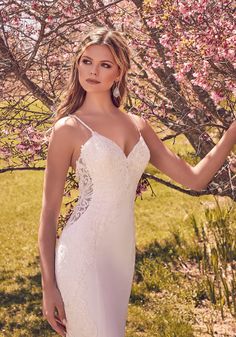 a woman in a white wedding dress standing next to a tree with pink flowers on it