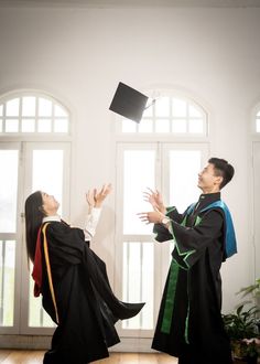 a man and woman in graduation gowns throwing their caps into the air