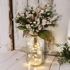 a vase with flowers and lights in it sitting on a white wooden table next to an old door